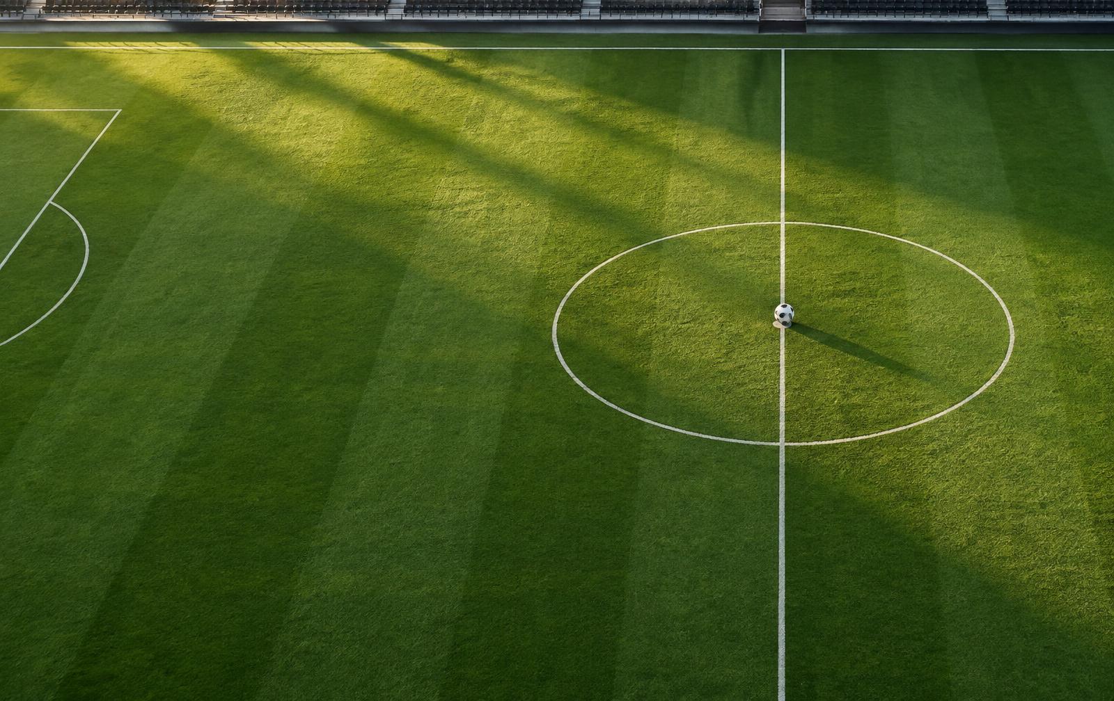 A football on the centre spot of a sunlit pitch